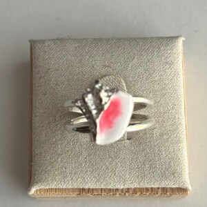 May include: A silver ring with a white and pink shell design. The ring has a double band and is set with small clear stones.