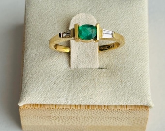 May include: A gold ring with a green emerald gemstone and two smaller diamonds on either side.