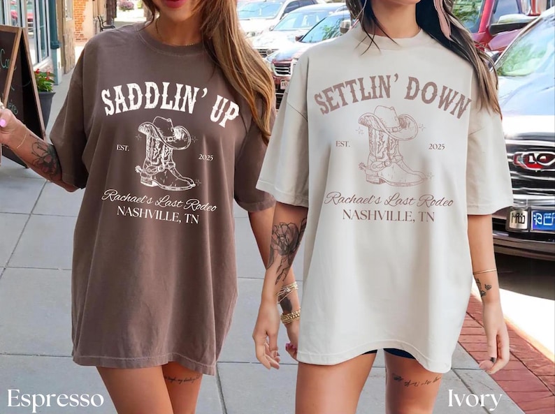 May include: Two oversized t-shirts, one espresso and one ivory, featuring a cowboy boot and hat graphic. The text reads "Saddlin' Up" and "Settlin' Down" with "Rachael's Last Rodeo, Nashville, TN".
