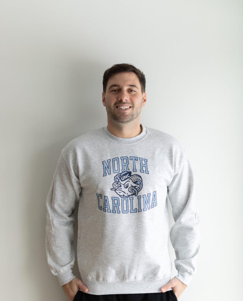 May include: A gray sweatshirt with a blue and white North Carolina Tar Heels logo. The logo features a ram's head with a UNC hat on top.