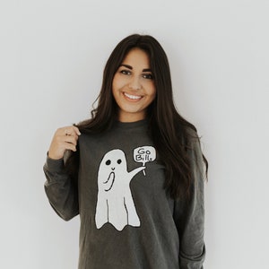 May include: A dark gray long-sleeved shirt with a white ghost graphic holding a sign that says "Go Bills".