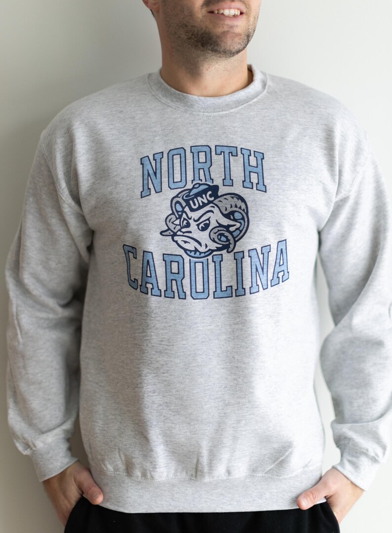May include: A gray sweatshirt with a blue and white North Carolina logo. The logo features a ram wearing a UNC hat.