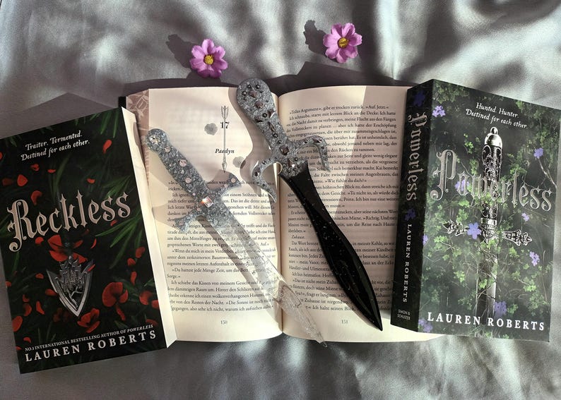Puede incluir: Dos libros de bolsillo de Lauren Roberts, "Reckless" y "Powerless", con el texto "Truiter. Tirmented Destined for each other" y "Hunted Hunter Destined for each other" en las portadas. Los libros est&aacute;n abiertos y tienen dos marcadores de daga decorativos plateados y negros.