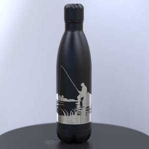 May include: Black insulated water bottle featuring a silver graphic of a fisherman. The bottle has a black cap and base. The fishing scene includes a person, fishing rod, water, and shoreline.