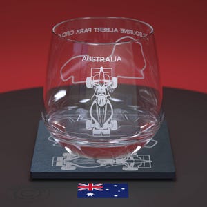 May include: A clear glass with an etched design of a racing car and the Albert Park Circuit in Melbourne, Australia. The glass is sitting on a black coaster with a similar design. The Australian flag is in the foreground.