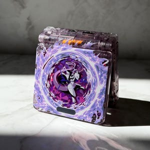 Può includere: Una console portatile per videogiochi con un guscio viola trasparente caratterizzato da una grafica del personaggio Mewtwo circondato da vorticosi effetti energetici viola e bianchi sulla cover frontale. Il dispositivo è in posizione chiusa.