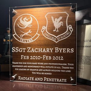 May include: A wooden plaque with etched white text and emblems. The plaque is dedicated to SSGT Zachary Byers, with dates Feb 2010-Feb 2012. The text includes a thank you message and the phrase "RADIATE AND PENETRATE".