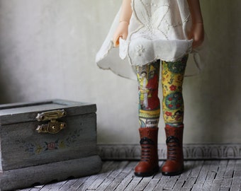 May include: A doll wearing a white dress and colorful patterned tights with brown boots. The doll is standing on a wooden floor.