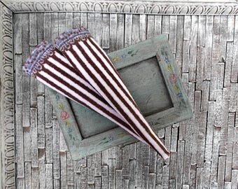 May include: A pair of brown and white striped leg warmers with a blue and white trim. The leg warmers are lying on a white wooden surface.