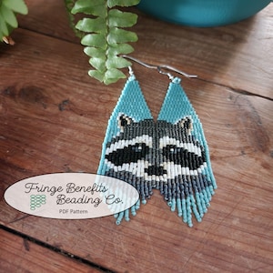 May include: A pair of beaded earrings featuring a raccoon face design. The earrings are made with turquoise, grey, white, and black beads. The earrings are hanging from silver ear wires. The earrings are labelled "Fringe Benefits Beading Co. PDF Pattern".