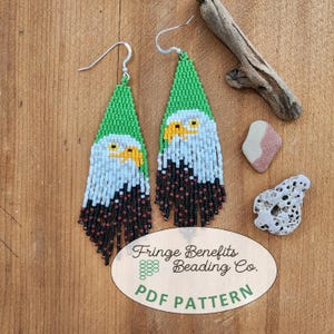 Pode incluir: Brincos de contas feitos à mão com um desenho de águia. Os brincos têm uma parte superior triangular verde, um corpo branco e azul e uma franja preta e castanha. O bico da águia é amarelo.