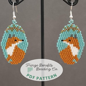 Pode incluir: Um par de brincos de contas com um design de raposa. A raposa é laranja, branca e marrom, e é cercada por contas turquesa. Os brincos estão pendurados em ganchos prateados.