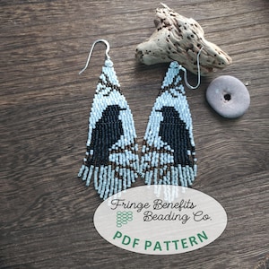 Könnte beinhalten: Handgefertigte Perlenohrringe mit einem schwarzen Vogeldesign auf hellblauem und braunem Hintergrund. Die Ohrringe haben unten Fransen. Das Bild enthält auch einen Holzuntergrund und ein Schild mit der Aufschrift "Fringe Benefits Beading Co. PDF Pattern."