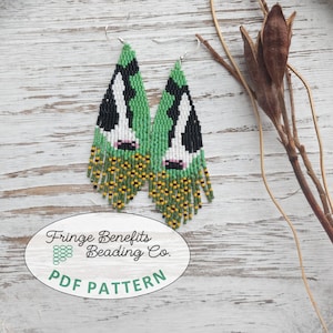 May include: A pair of beaded fringe earrings featuring a cow pattern in black, white, and green, with yellow and black fringe at the bottom. An oval label reads Fringe Benefits Beading Co. PDF PATTERN with a small green bead icon.