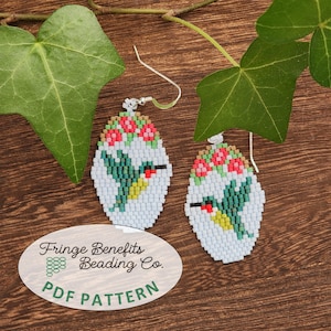 Op de afbeelding: Een paar kralen oorbellen met een kolibrie ontwerp. De oorbellen zijn ovaal, met een lichtblauwe achtergrond en een gedetailleerde kolibrie in groen, geel en rood. De bovenkant van de oorbellen heeft rode en roze bloemen. De tekst "Fringe Benefits Beading Co. PDF PATTERN" is zichtbaar.