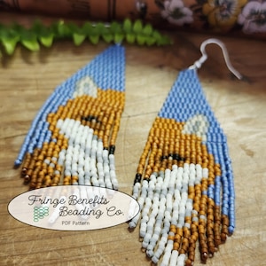 May include: A pair of beaded earrings with a fox design. The earrings are blue, brown, white, and black. The earrings are fringe style and have a long, dangling design. The earrings are labeled "Fringe Benefits Beading Co. PDF Pattern".