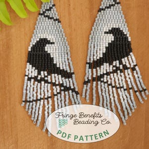 May include: A pair of long, black and white beaded earrings with a fringe design. The earrings are in the shape of a teardrop and feature a black bird design. The earrings are hanging from a wooden surface. The text "Fringe Benefits Beading Co. PDF PATTERN" is visible in the image.