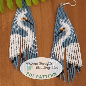 Puede incluir: Un par de pendientes de cuentas azules y blancas con un diseño de pájaro blanco. Los pendientes cuelgan de ganchos de oreja plateados. Los pendientes están etiquetados como "Fringe Benefits Beading Co. PDF Pattern".