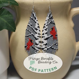 May include: Handmade beaded earrings with a grey, white, and black pattern, featuring two red cardinal bird designs. The earrings have a fringe at the bottom and are displayed against a neutral background. The earrings are a PDF pattern.
