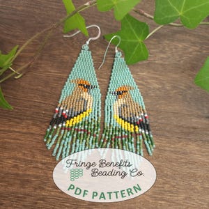 May include: Handmade beaded earrings with a teal background and a bird design. The earrings have a fringe at the bottom and silver hooks. The bird is depicted in shades of brown, yellow, and gray. The earrings are labeled "Fringe Benefits Beading Co. PDF Pattern."
