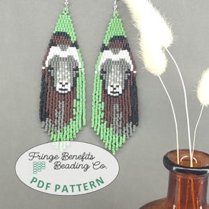 May include: A pair of long, teardrop-shaped beaded earrings featuring a musk ox design in shades of brown, gray, white, and green. The earrings have a fringe bottom and silver-toned hooks. A white oval label displays the text Fringe Benefits Beading Co. PDF PATTERN.