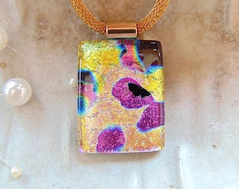 May include: A gold chain necklace with a rectangular glass pendant. The pendant has a yellow, pink, and purple abstract design with black accents.