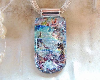 May include: A dichroic glass pendant necklace with a silver chain. The rectangular pendant features a blend of blues, purples, and silver, creating a shimmering effect. The necklace is a piece of jewellery.