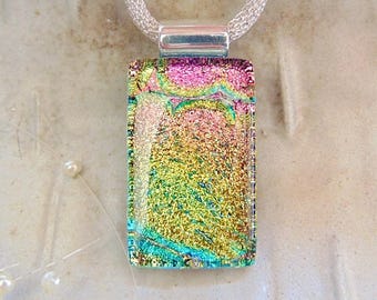 May include: A rectangular dichroic glass pendant featuring a vibrant blend of iridescent gold, pink, and teal colors. The pendant is suspended from a silver-toned metal bail and a textured silver-toned mesh chain necklace.