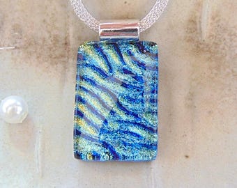 May include: A rectangular pendant necklace with a dichroic glass design in shades of blue and yellow. The pendant is suspended from a silver mesh chain. A pearl is visible in the background.