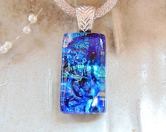 May include: A rectangular dichroic glass pendant featuring vibrant shades of blue and teal with iridescent flecks. The pendant is suspended from a silver-toned woven mesh chain by a textured, chevron-patterned metal bail, creating a cohesive piece.