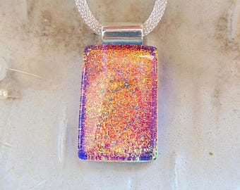 May include: A rectangular dichroic glass pendant featuring a vibrant blend of orange, pink, and purple hues with a shimmering, textured surface. The pendant is suspended from a silver-toned metal mesh chain by a polished silver-toned bail.