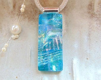 May include: A rectangular dichroic glass pendant in shades of blue and turquoise with iridescent silver accents. The pendant is suspended from a silver-toned mesh chain and features a smooth, glossy finish with a reflective, multi-layered appearance.