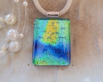 Puede incluir: Un collar de cadena de plata con un colgante rectangular de vidrio dicroico. El colgante tiene un acabado iridiscente azul, verde y amarillo.
