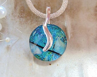 May include: A circular dichroic glass pendant featuring vibrant blue and green hues with black linear accents. The pendant is suspended from a silver-toned wavy bail attached to a textured silver-toned mesh chain necklace.