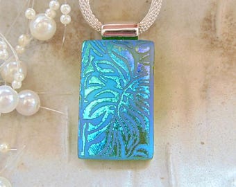 May include: A rectangular dichroic glass pendant featuring a vibrant blue and green leaf pattern. The pendant is suspended from a silver-toned mesh chain and is accented by a silver-toned bail at the top, creating a reflective and colourful jewellery piece.