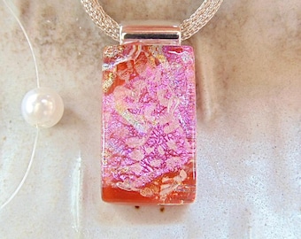 May include: A rectangular pendant necklace with a silver chain. The pendant features a pink and red dichroic glass design. A white pearl is visible on a thin string to the left of the pendant.