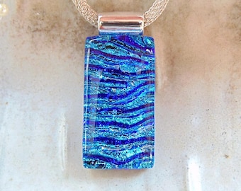 May include: A rectangular pendant with a blue and purple wave pattern, suspended from a silver chain. The pendant has a metallic silver clasp. The design evokes a sense of water or ocean waves. Jewelry.