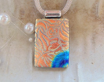 May include: A silver chain necklace with a rectangular pendant featuring a blue and copper iridescent glass design with a floral pattern.