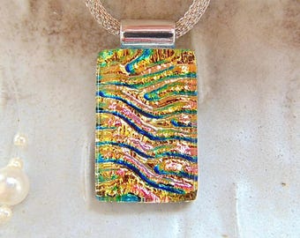 May include: A rectangular pendant with a colourful, layered glass design in shades of gold, blue, green, and pink. The pendant is suspended from a silver chain. The glass has a textured, wave-like pattern. The pendant is approximately 2.5 cm in length.