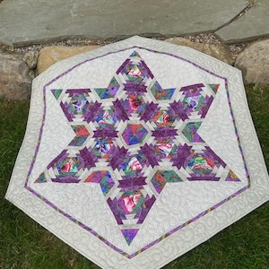 May include: A white hexagonal quilt with a purple and green star design. The star is made up of smaller stars and has a floral pattern.