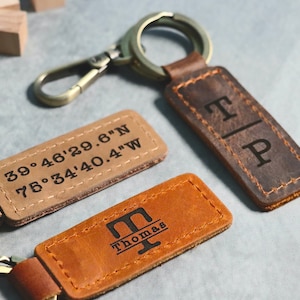 May include: Two leather keychains with engraved designs. One keychain has the coordinates "39.46'29.6"N 75.34'40.4"W" engraved on it. The other keychain has the initials "T|P" engraved on it.