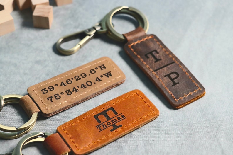 May include: Two leather keychains with engraved designs. One keychain has the coordinates "39.46'29.6"N 75.34'40.4"W" engraved on it. The other keychain has the initials "T|P" engraved on it.