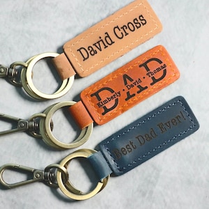 May include: Three leather keychains with metal rings and clasps. The keychains have different colors and personalized text: "David Cross", "DAD Kimberly David Thomas", and "Best Dad Ever!"