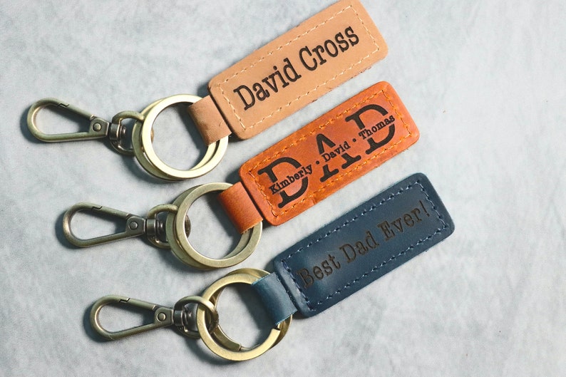 May include: Three leather keychains with metal rings and clasps. The keychains have different colors and personalized text: "David Cross", "DAD Kimberly David Thomas", and "Best Dad Ever!"