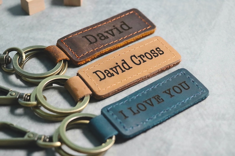 May include: Three leather keychains with metal rings. The first keychain is brown and says "David". The second keychain is tan and says "David Cross". The third keychain is blue and says "I Love You".