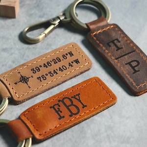 May include: Two leather keychains with engraved initials and coordinates. One keychain is brown with the initials "T|P" and the other is tan with the initials "FBY" and the coordinates "39°46'29.6"N 75°34'40.4"W".
