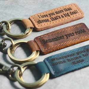 May include: Three leather keychains with different engraved messages. The first keychain is brown and says "I love you more than cheese, that's a big deal!" The second keychain is brown and says "Remember your roots". The third keychain is blue and says "Wherever you go, home home to me - Kate".