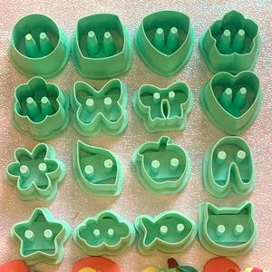 Peut inclure: Ensemble de découpoirs à biscuits en plastique vert de différentes formes : cercles, coeurs, fleurs et animaux. Sont également présentées des décorations en fondant colorées, dont des boutons, des feuilles et un papillon.