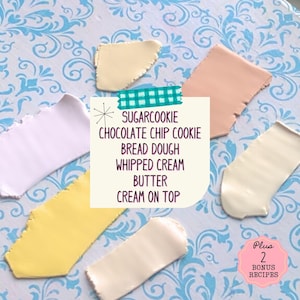 Op de afbeelding: Zes verschillende gekleurde stukken modelleerklei, gerangschikt in een rij op een blauw-wit gepatroneerd oppervlak. De klei is gelabeld met de tekst: "SUGARCOOKIE CHOCOLATE CHIP COOKIE BREAD DOUGH WHIPPED CREAM BUTTER CREAM ON TOP". De tekst "Plus 2 BONUS RECIPES" is ook zichtbaar in de afbeelding.