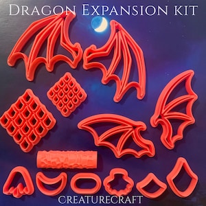 May include: A set of orange plastic cookie cutters and a texture roller labelled DRAGON EXPANSION KIT and CREATURECRAFT. The collection includes various dragon wing shapes, diamond-patterned scales, and several small geometric and organic shapes.